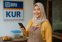 Seorang pelaku UMKM tersenyum sambil memegang smartphone di depan papan bertuliskan KUR BRI. Program KUR BRI 2025 terus mendukung pengusaha kecil dan menengah dengan pembiayaan mudah dan bunga rendah, mendorong pertumbuhan ekonomi masyarakat.
