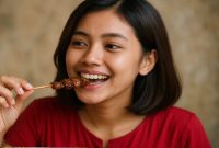 Seorang perempuan memakan Sate yang menjadi  salah satu Rekomendasi Makanan Khas Indonesia