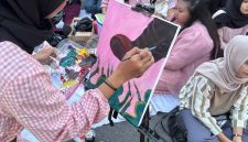 Seorang pelukis wanita di Kota Medan bernama Amanda Gustaro sedang melukis sepatu boot sebagai simbol kekerasan, di tengah kerumunan aksi Women’s March Medan, Sabtu (6/9).