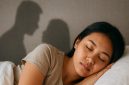 Seorang perempuan muda sedang tertidur dengan gelisah, sementara bayangan suaminya terlihat sedang selingkuh dengan mantan. Ilustrasi ini menggambarkan keresahan dan kecemasan yang muncul dalam mimpi, sesuai dengan tafsir dan arti mimpi suami selingkuh dengan mantan menurut primbon Jawa maupun psikologi modern.