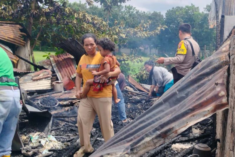Seorang ibu memeluk erat anaknya sambil berjalan di antara puing-puing kios yang hangus terbakar di Jalan Marindal, Deli Tua, Senin (13/10/2025). Foto : Topikseru.com/Mangara Wahyudi